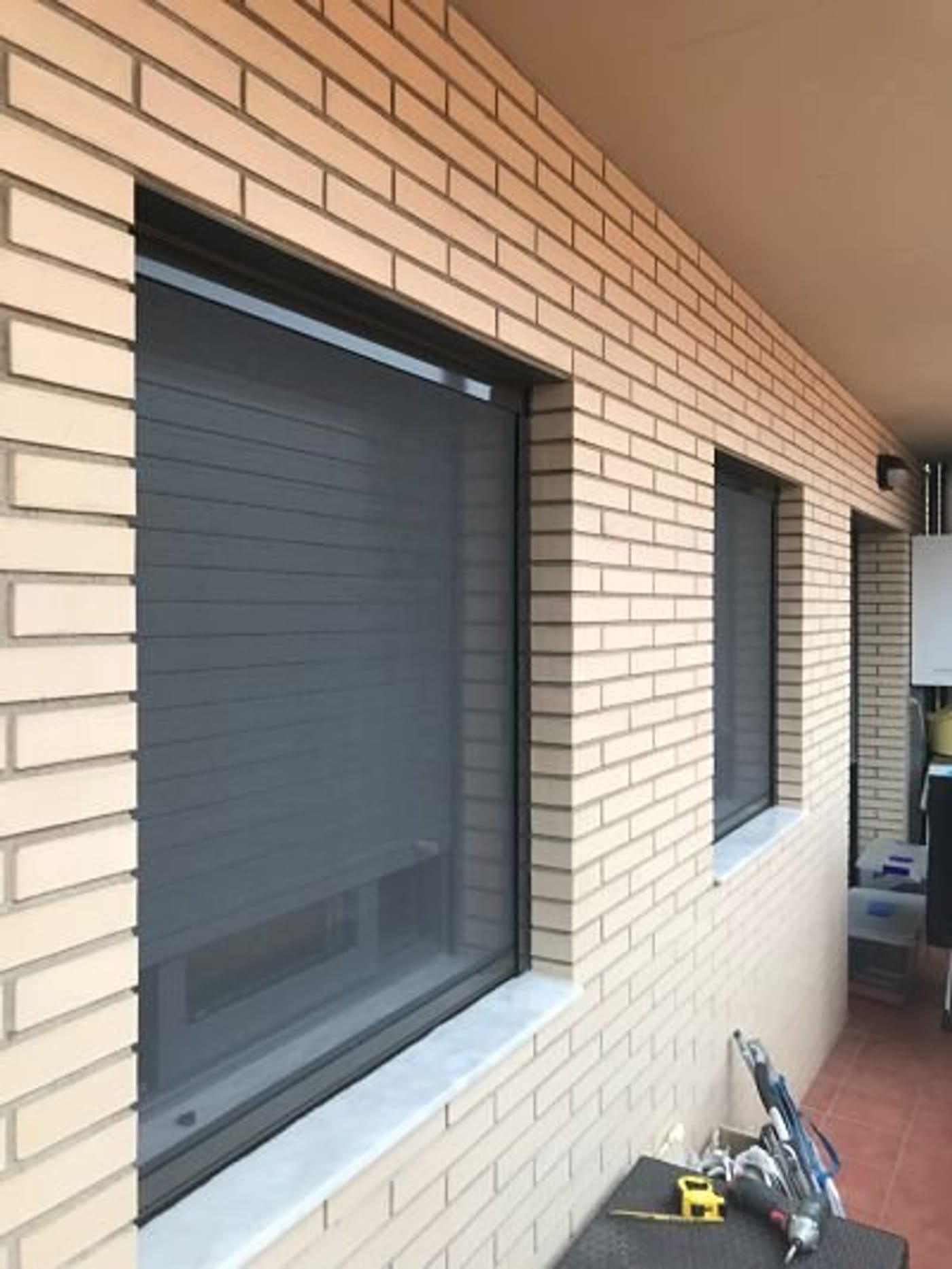 Persiana de aluminio gris instalada en una fachada de ladrillo por Repara Persiana